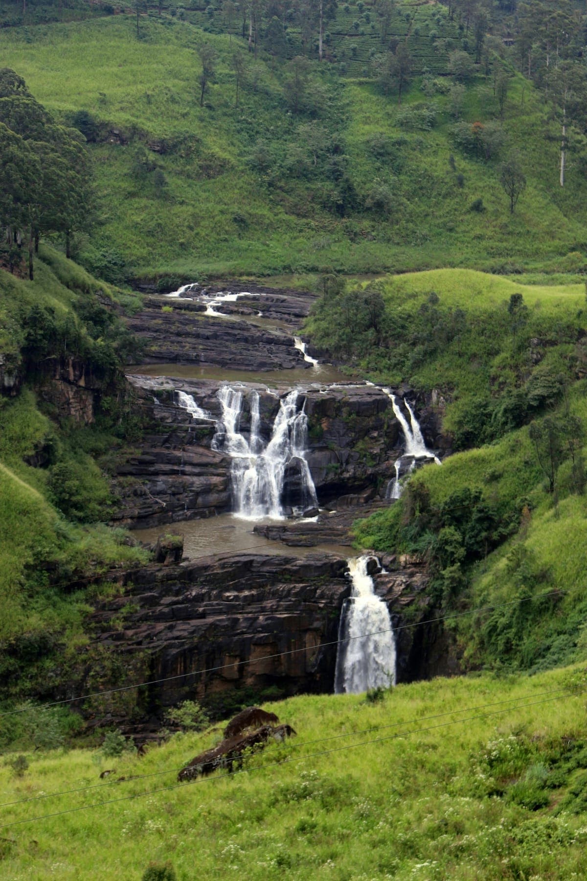 A multi-tier waterfall threading through lush green hill country